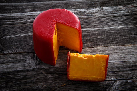 Round red cheese gem with a slice cut out on a wooden surface