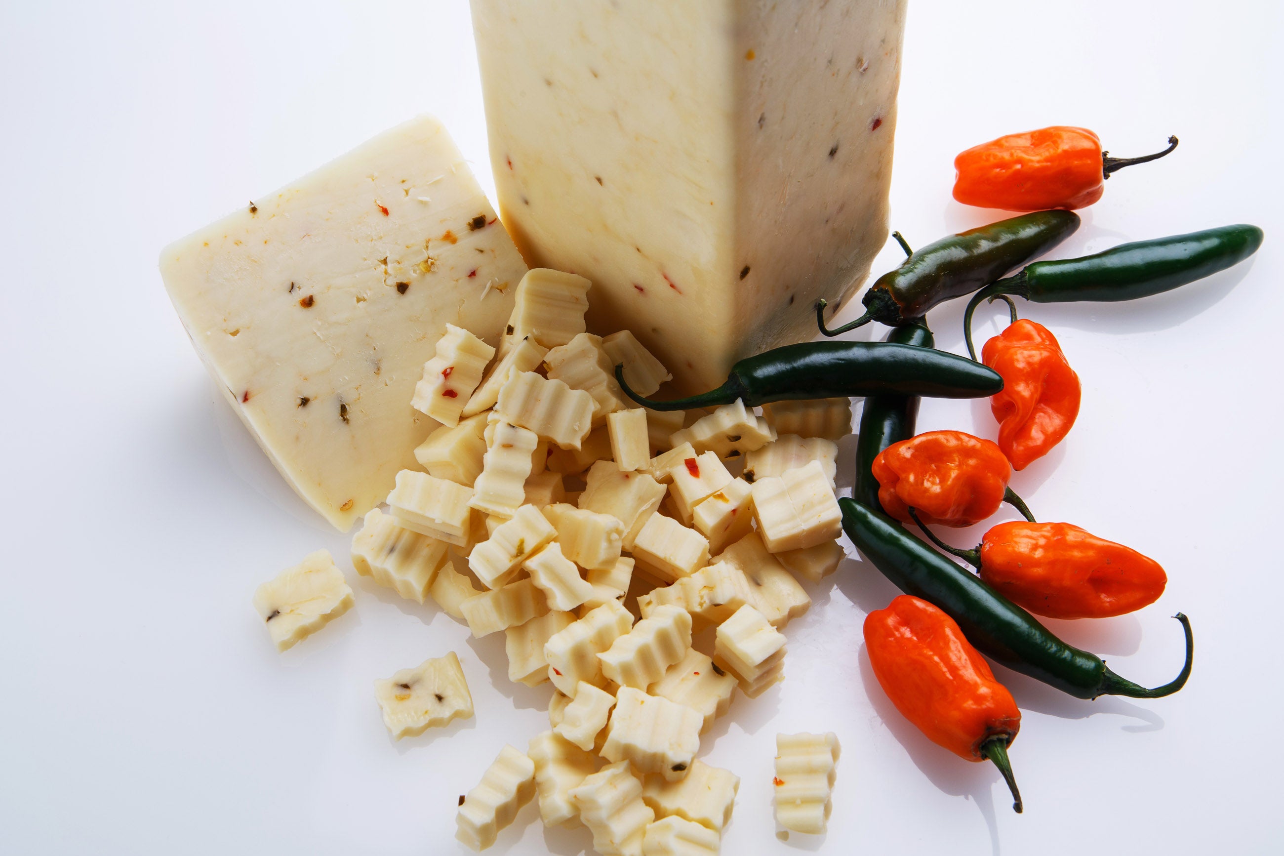 Pepper jack cheese is cubed and shredded, surrounded by red and green peppers, against a white background