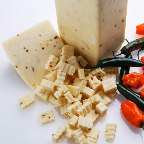 Pepper jack cheese is cubed and shredded, surrounded by red and green peppers, against a white background